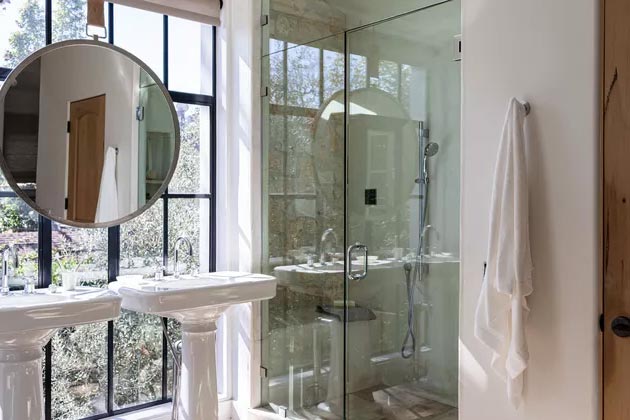 Ванная комната с большими окнами, фарфоровыми раковинами, большим зеркалом и душевой кабиной со стеклянной дверью